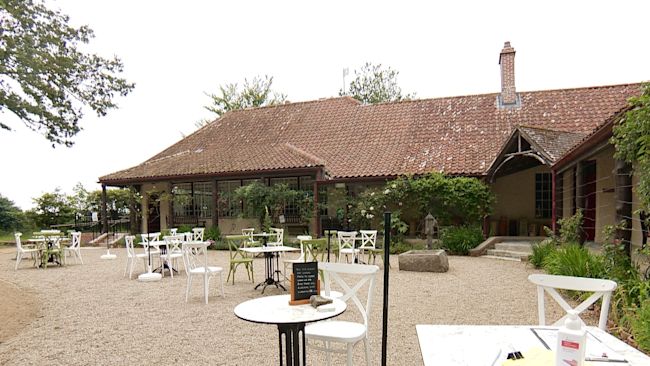 Tables and chairs on gravel outside an old building with a bottle of hand sanatiser on a table on the right of the picture