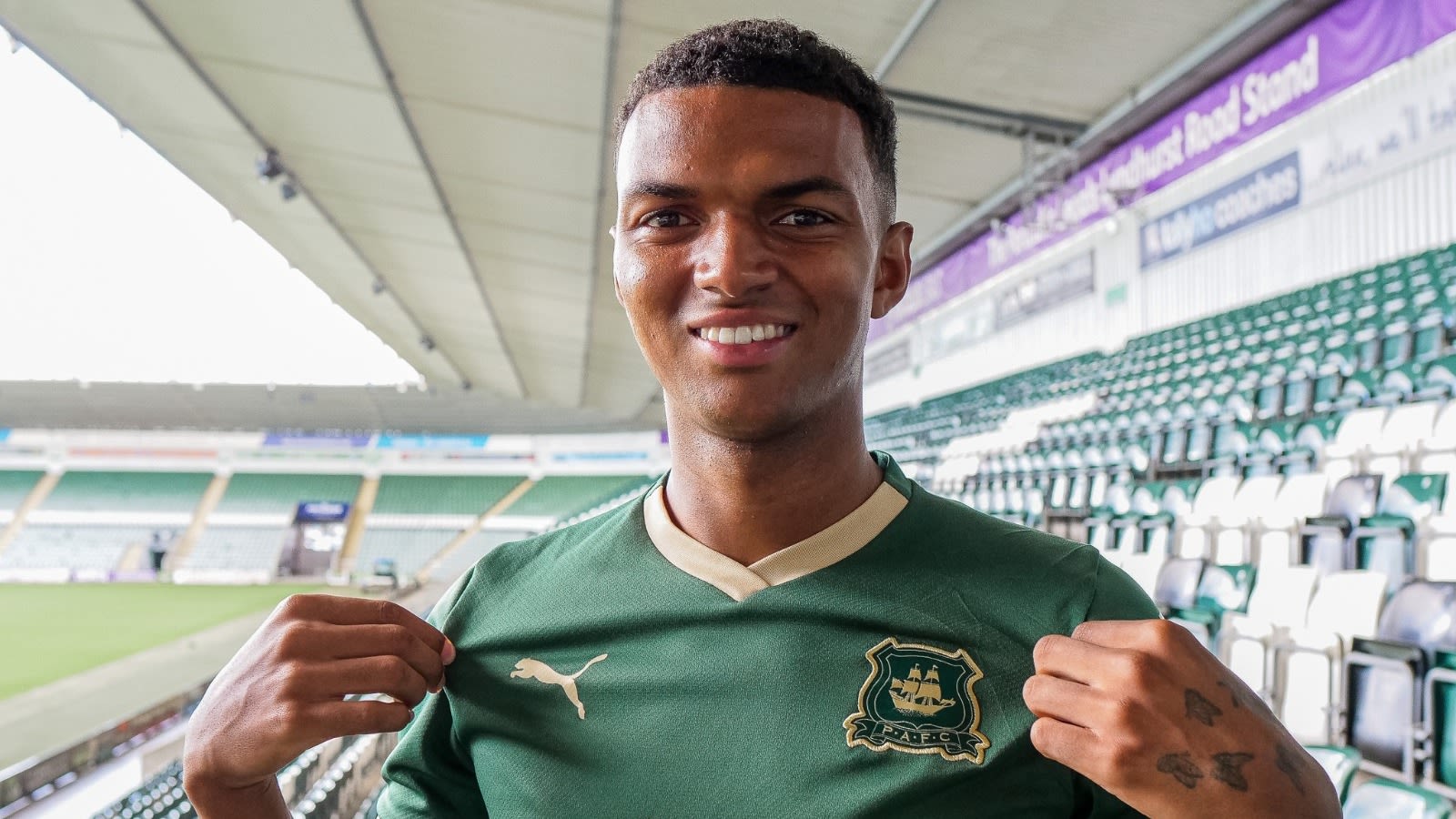  Morgan Whittaker, a Plymouth Argyle forward, is pictured smiling in a green jersey with gold trim, holding the team crest on the front.