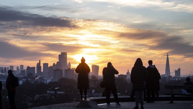 A small crowd of people watch as the sun rises over the city skyline from Primrose Hill, London.…