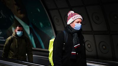 Commuters in a London underground tube station wearing face coverings