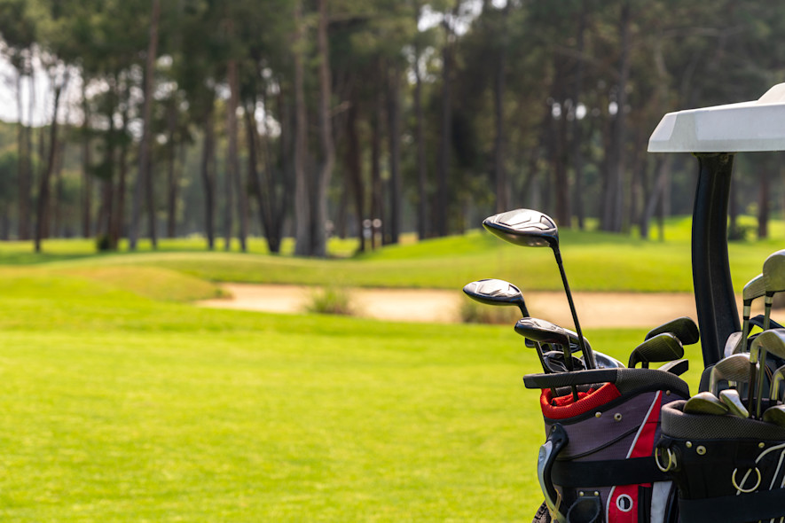 Close-up of golf clubs carried inside a golf car. In the background, a golf course.