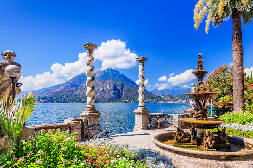 The exterior of a historic villa on Lake Como with the surrounding mountains in the background