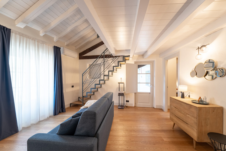 Porzione del salone con divano, madia e decorazioni alle pareti di uno degli appartamenti all'interno di Palazzo Odescalchi a Como, gestito da Wonderful Italy.