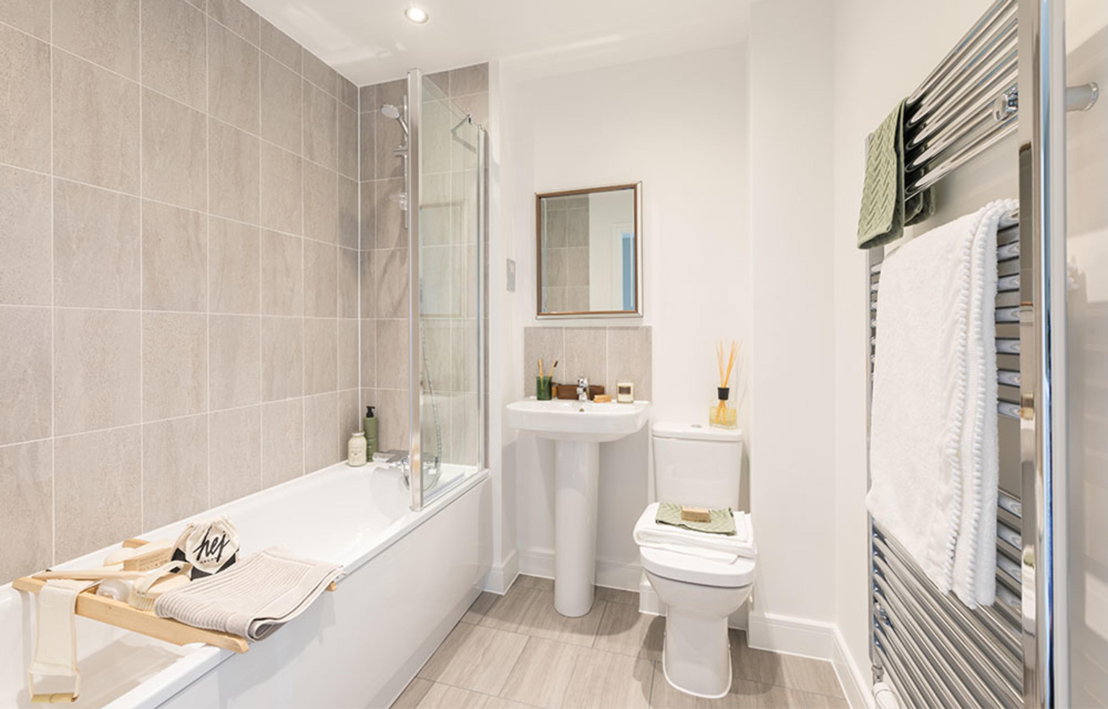 Neutral coloured tiled bathroom with bath and over bath shower