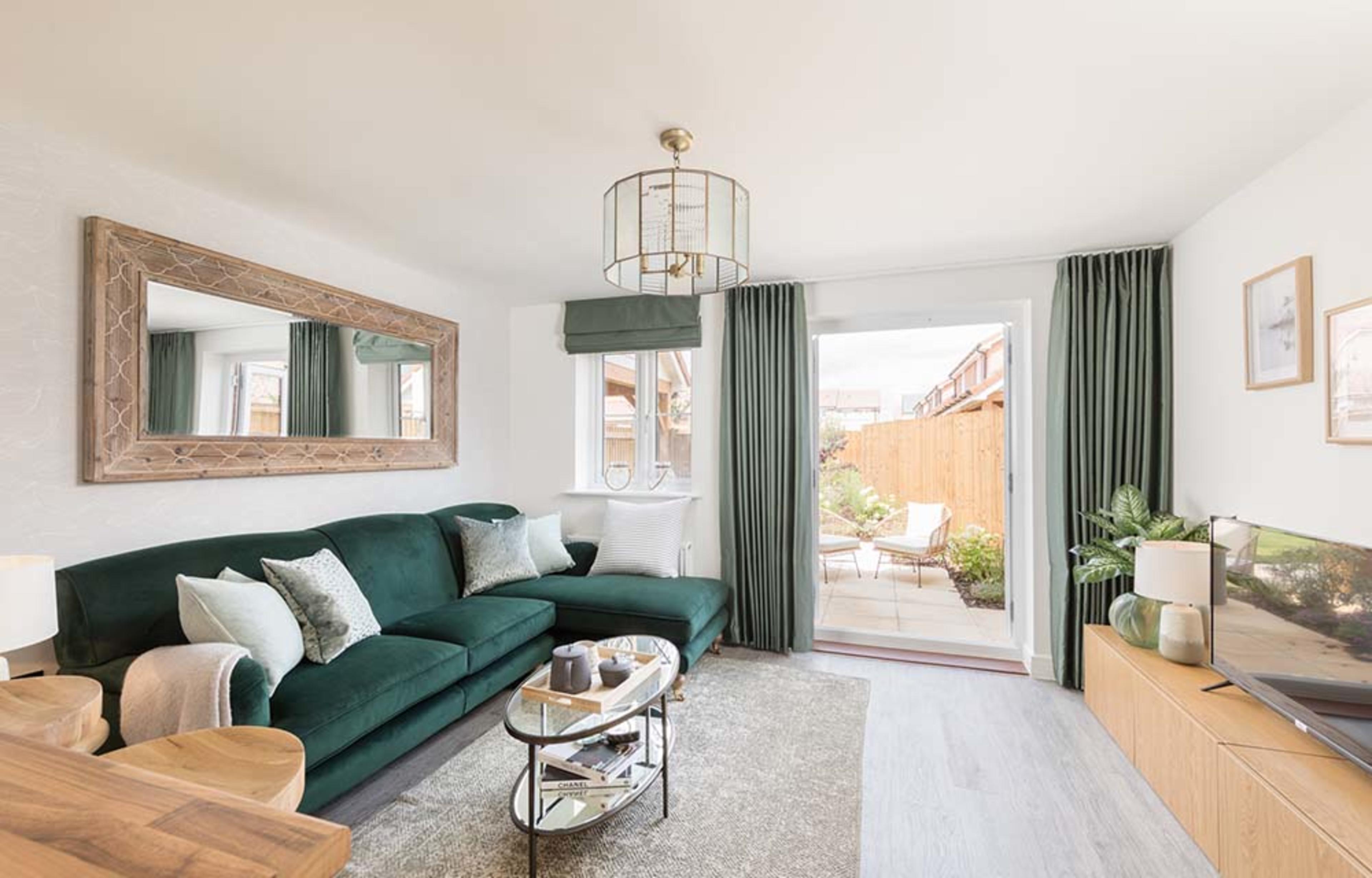 A neutral-coloured living room with emerald green sofa, natural wood cabinets and sideboard, and French doors opening onto the rear garden.