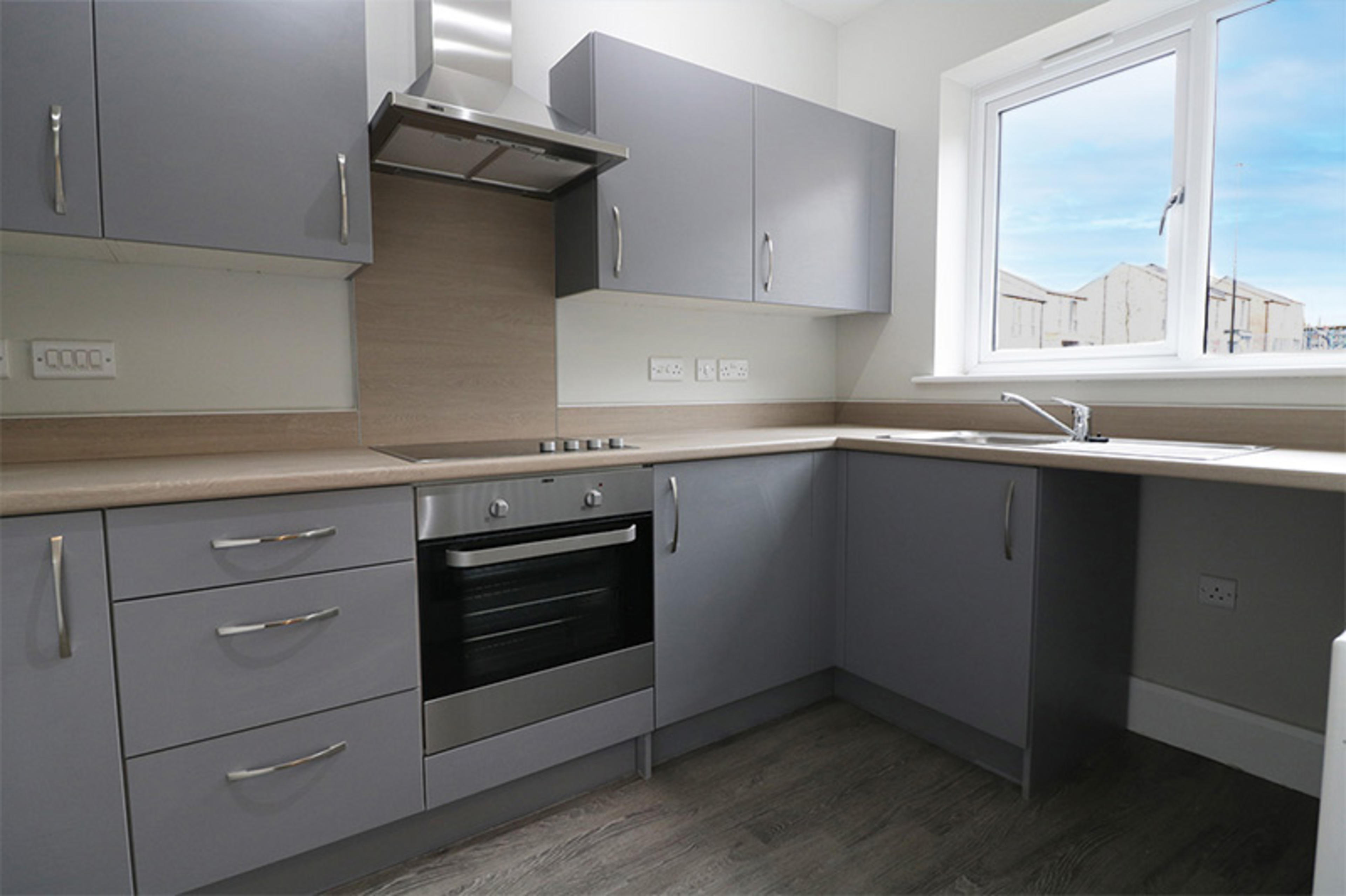 A blue-grey L-shaped kitchen with beechwood worktops and silver oven/cooker hood