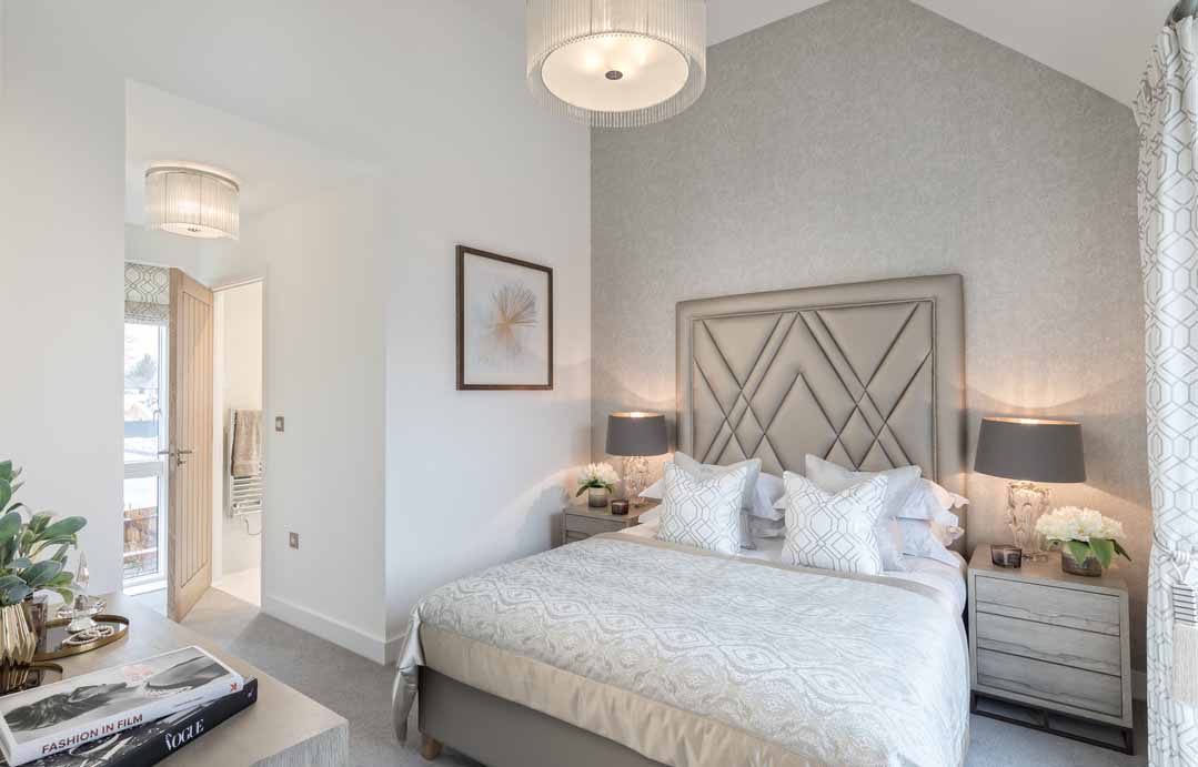 Bedroom with double bed, hanging lights and bedside drawers with matching grey table lamps. A door leads into an en-suite bathroom.