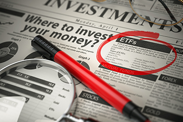 Newspaper with ETF's circled in red, a red pen and a magnifying glass on top
