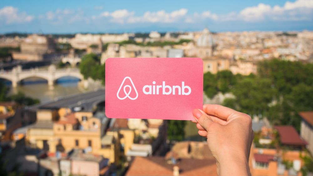 A person holding Airbnb logo in Rome, Italy.  Image Credit: Kaspars Grinvalds, Shutterstock.