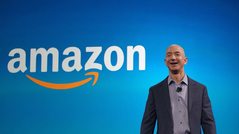 Amazon CEO Jeff Bezos laughs in front of the company's logo.