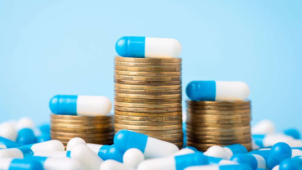 Stacks of coins between medical pills capsules. Image credit: Vitalii Petrushenko/Getty Images