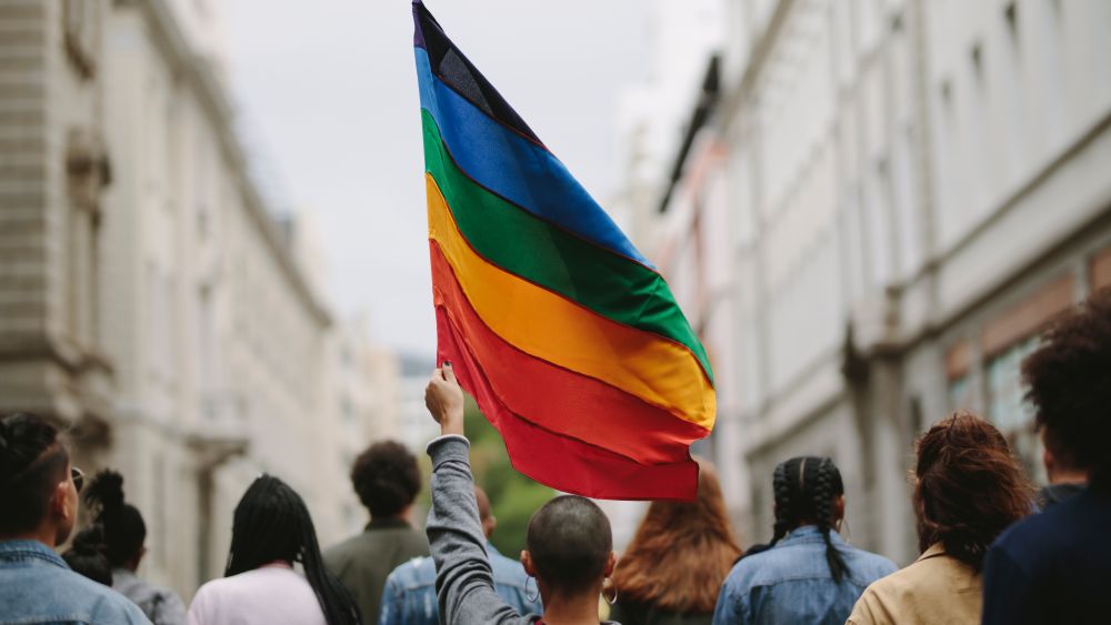 Group of people on the city street with gay rainbow flag. Image courtesy of Jacob Lund via Shutterstock.