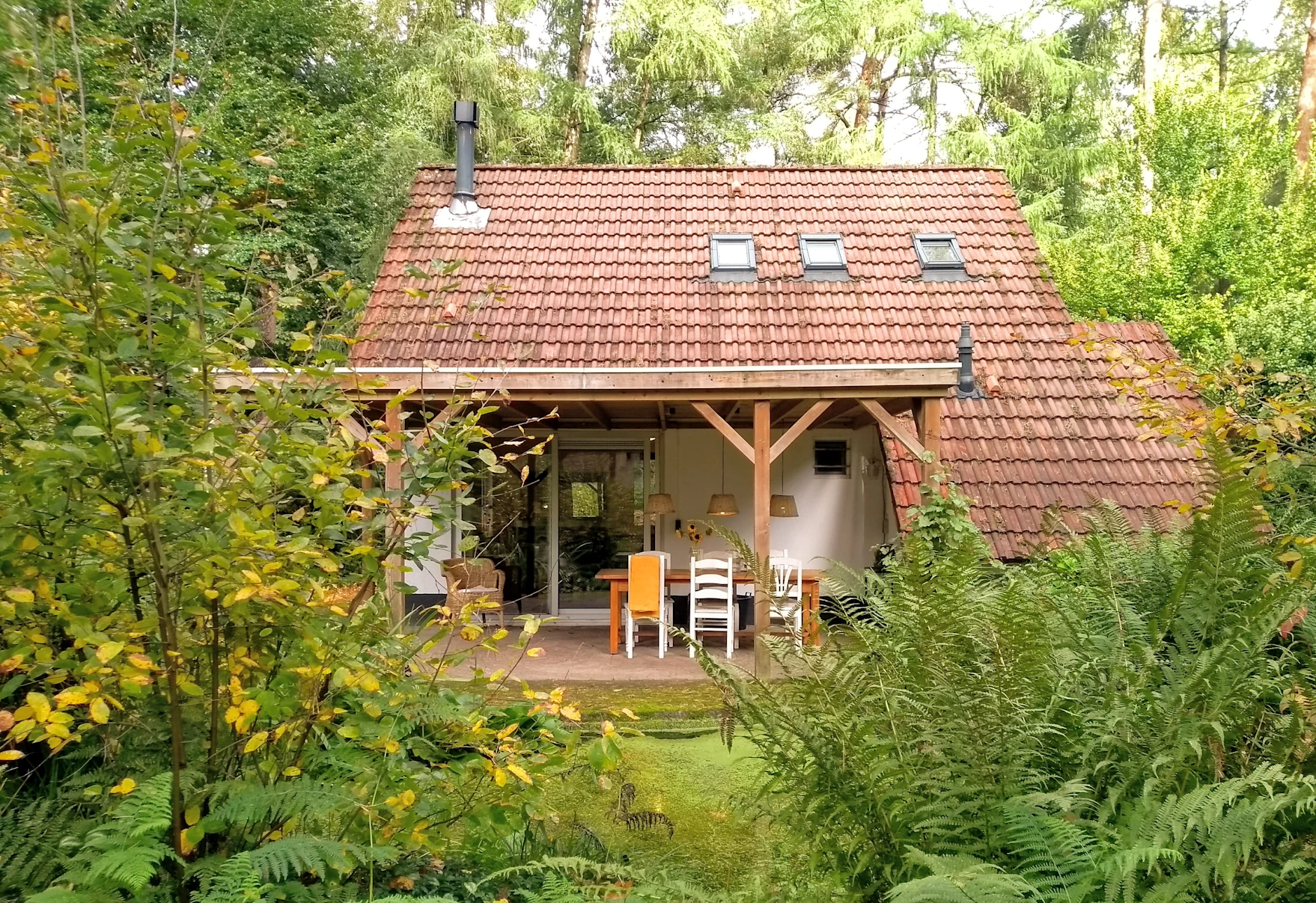 Une petite maison blanche dans un bois verdoyant, avec un porche et des chaises