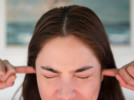 Woman plugging ears and squinting eyes trying to block out sound