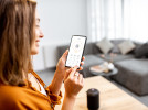 Woman holding smartphone with home security app open with settings showing on screen.