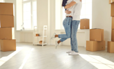 A man and woman embrace in a room full of brown boxes