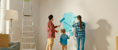 A man, woman and young girl apply bright blue paint to a white wall.