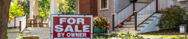 A 'for sale' sign in front of a house with a patio, flowers and stairs