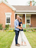 Young couple standing in front of red brick rambler home.