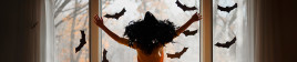 A young girl reaches out to a window with black bats attached near Halloween