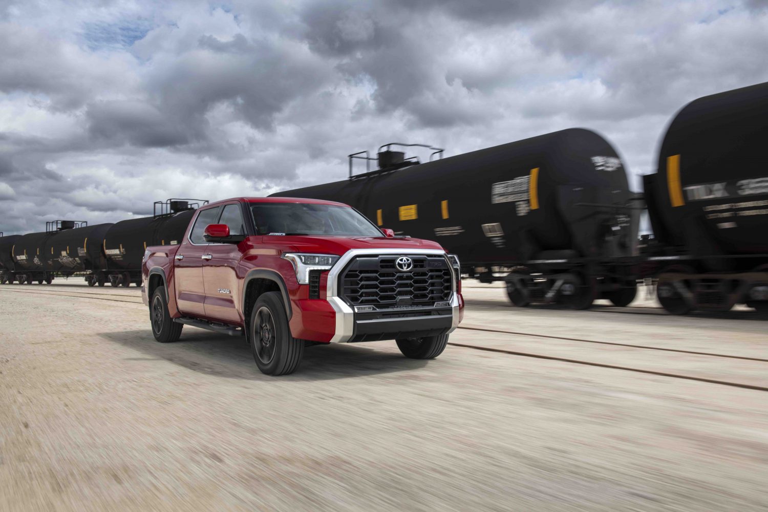 a red 2022 Toyota Tundra Limited driving near a train