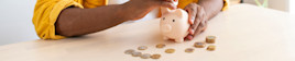 A man puts coins into a small, pink piggy bank.