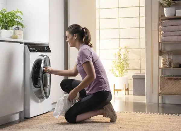 Une femme à genoux chargeant un sèche-linge.