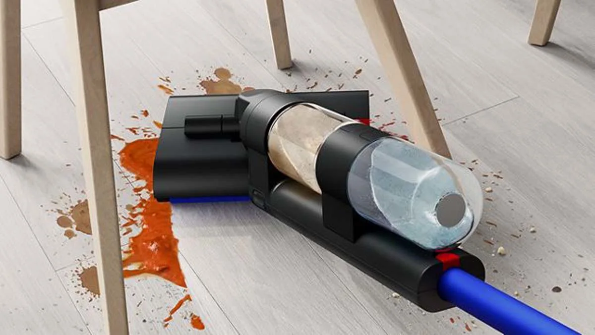 Une utilisatrice faisant glisser le nettoyeur de sols durs Dyson WashG1 pour éliminer de grandes éclaboussures de nourriture sous une chaise