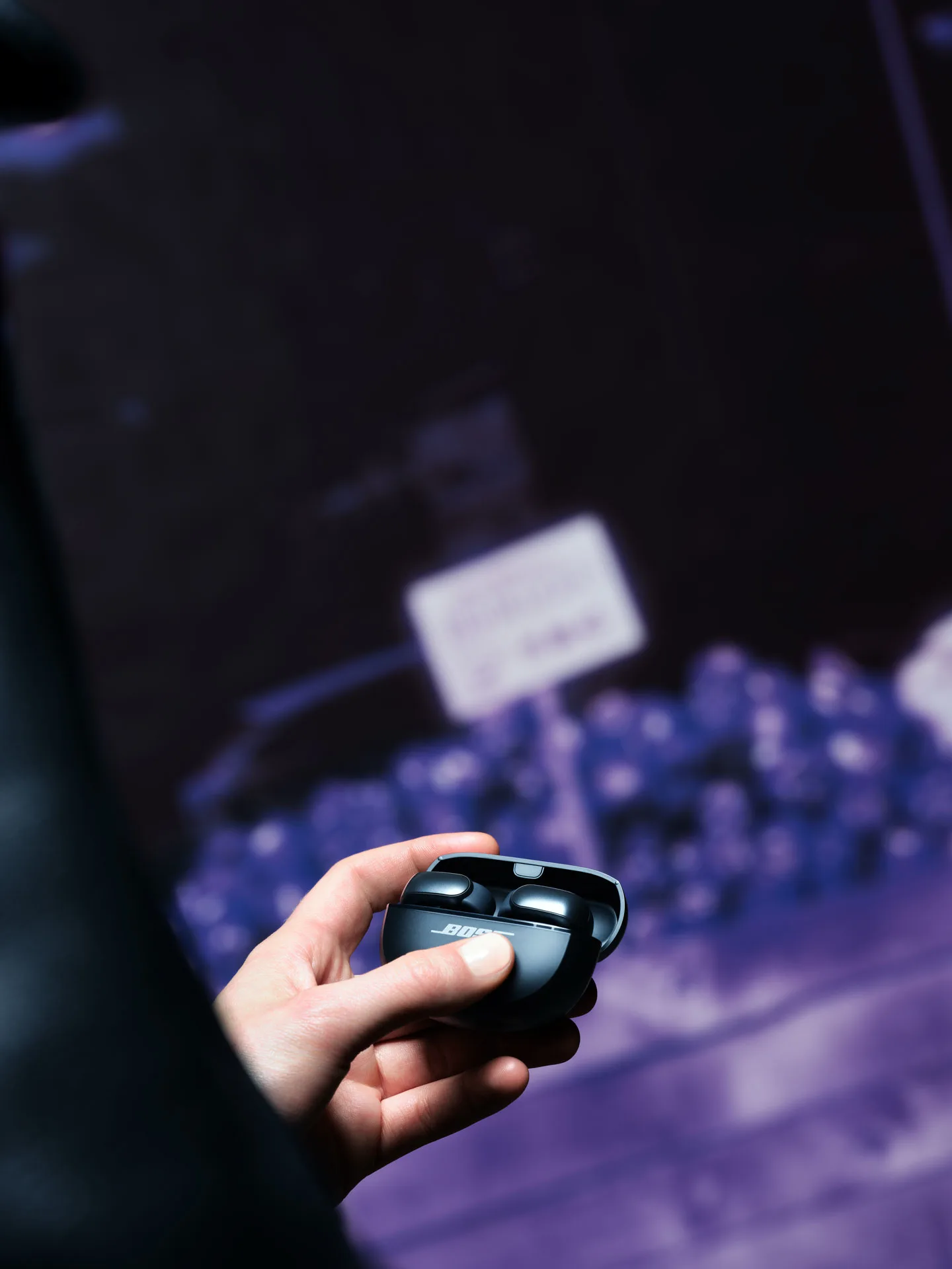 A person holding black Wireless Bose Open Ultra Earbuds.