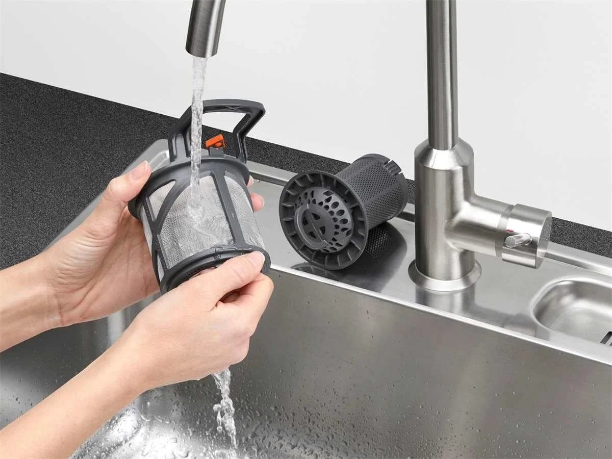 A person washing a dishwasher filter.