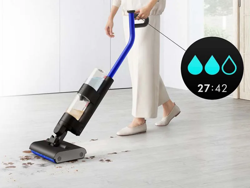 Een gebruiker maakt een harde vloer in een woonkamer schoon, terwijl waterdruppels op het lcd-scherm bevochtigingsstand 1 aangeven