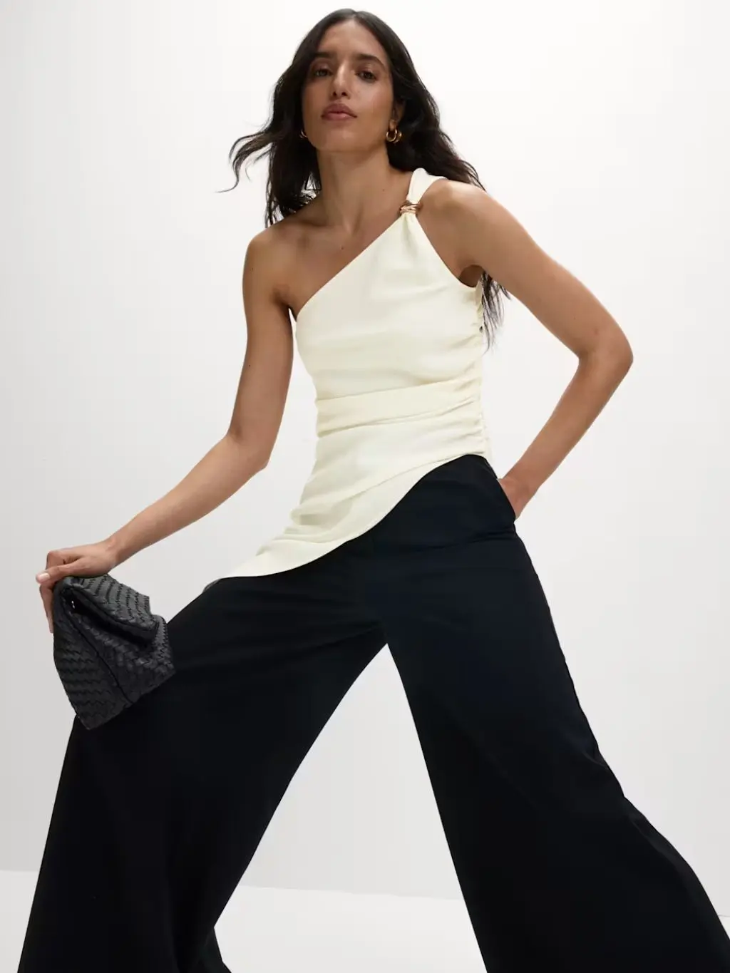A woman wears a cream asymmetric top with black wide-leg trousers