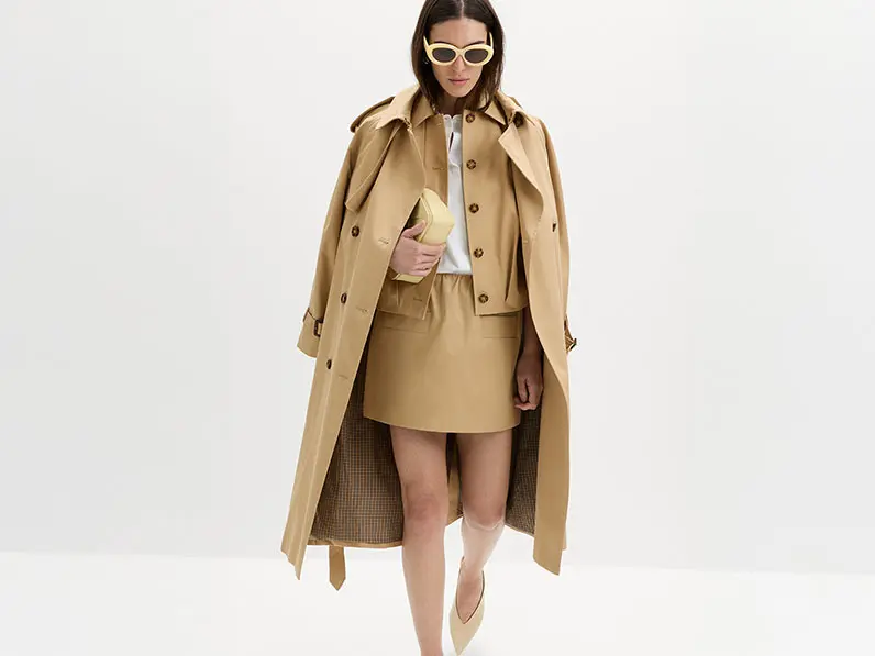 Woman wearing a balloon-sleeve jacket with a white shirt, coordinating skirt, long trench, and yellow accessories