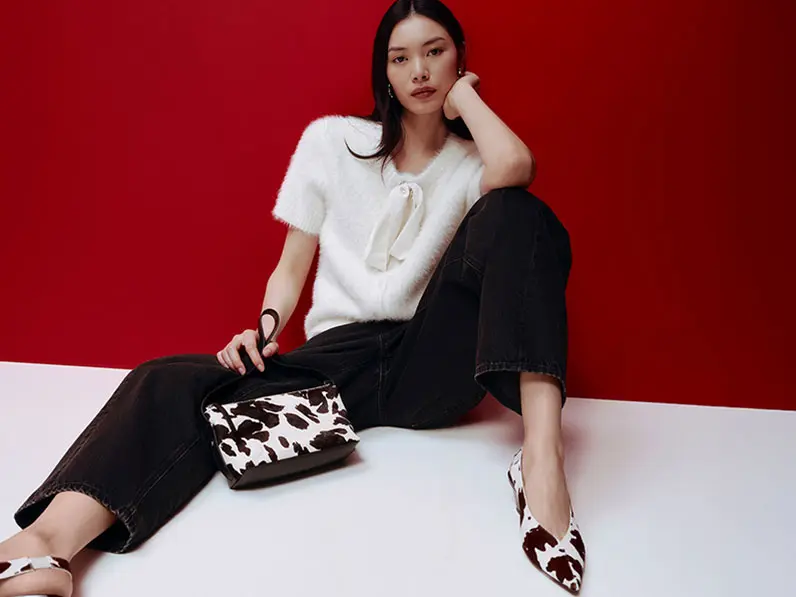 Woman wearing a white bow-detail cardigan with black jeans, cow-print heels and a cow-print bag