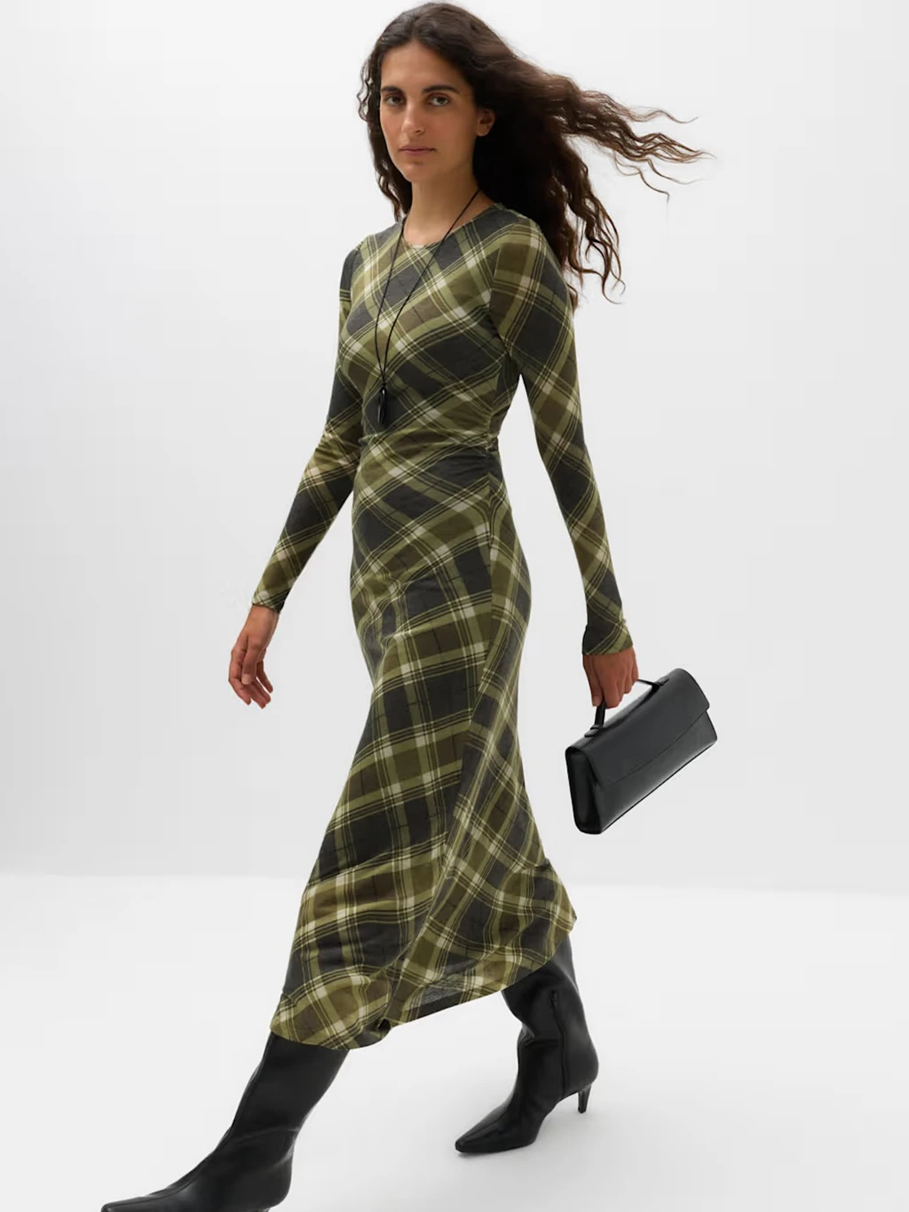 Woman in a green checked midi dress, knee-high black boots and black handbag.