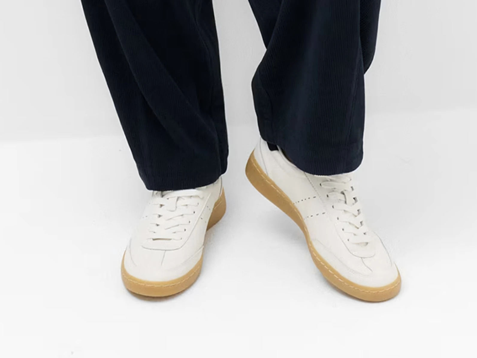Close up of a woman wearing blue trousers and white trainers with a gum sole.