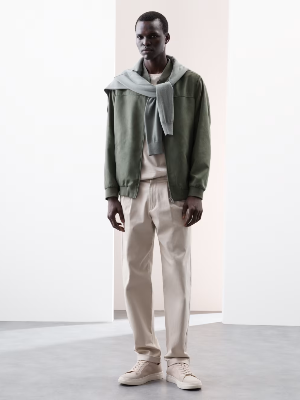 A man wears a light green suede bomber jacket with light chinos