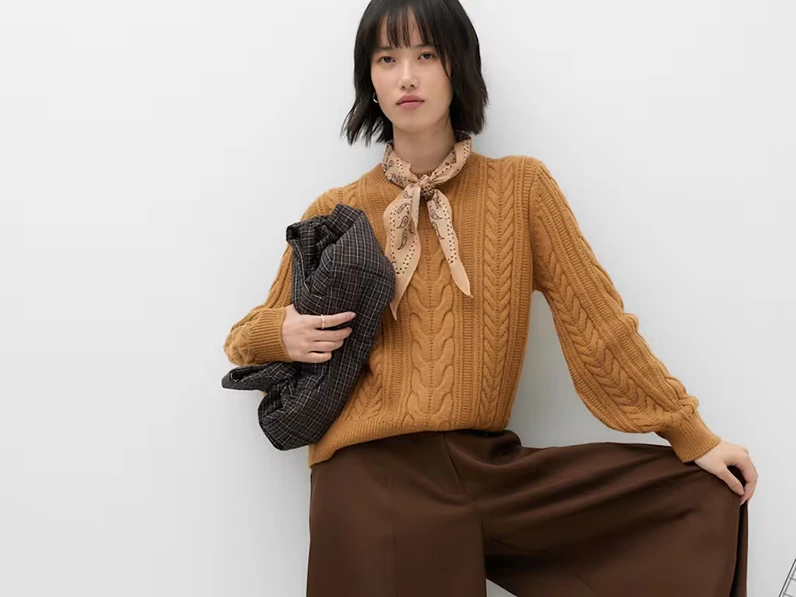 Woman wearing brown trousers with a burnt orange cable knit jumper.