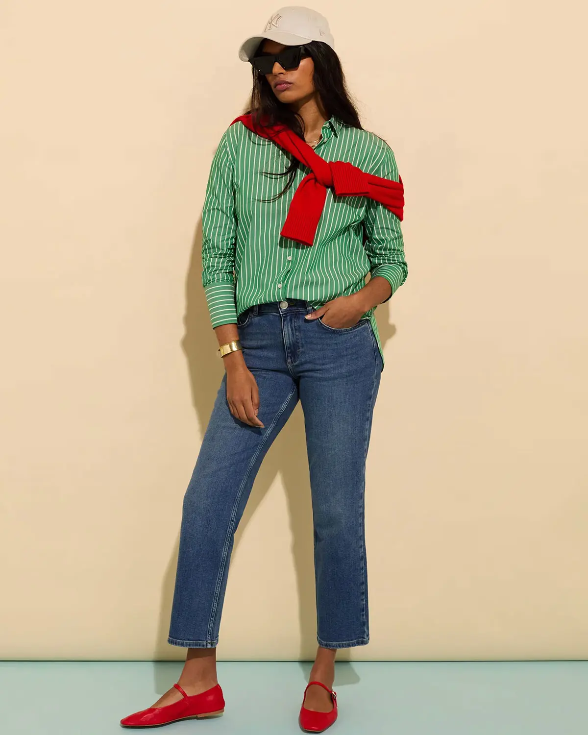 Woman wearing green striped shirt, blue skinny jeans, red ballet flats and cream cap