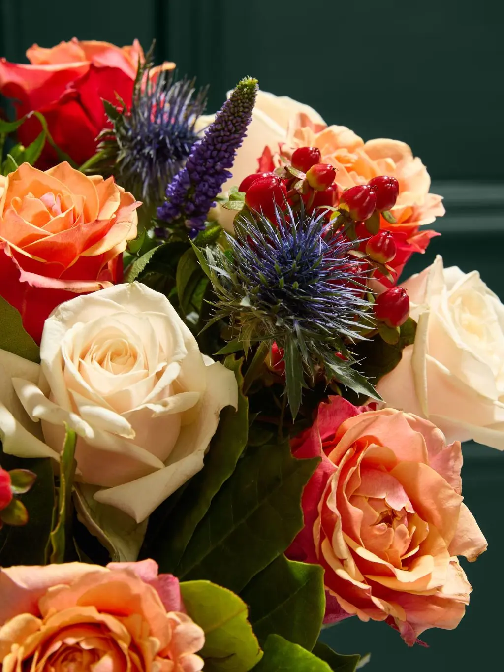 A close up of an autumn bouquet containing roses and sea holly
