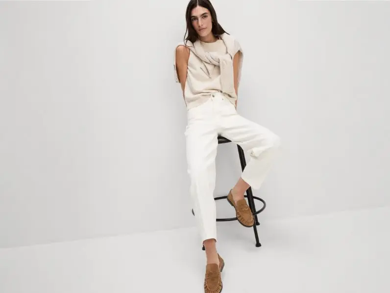 A woman wears a cream top and cream jeans with suede tan loafers