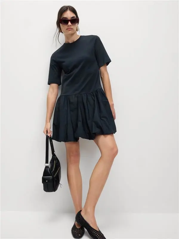 Woman wearing a navy mini dress with black ballet pumps, sunglasses and a black handbag.