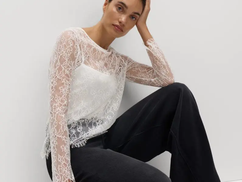 A woman wears a white lace top and black jeans