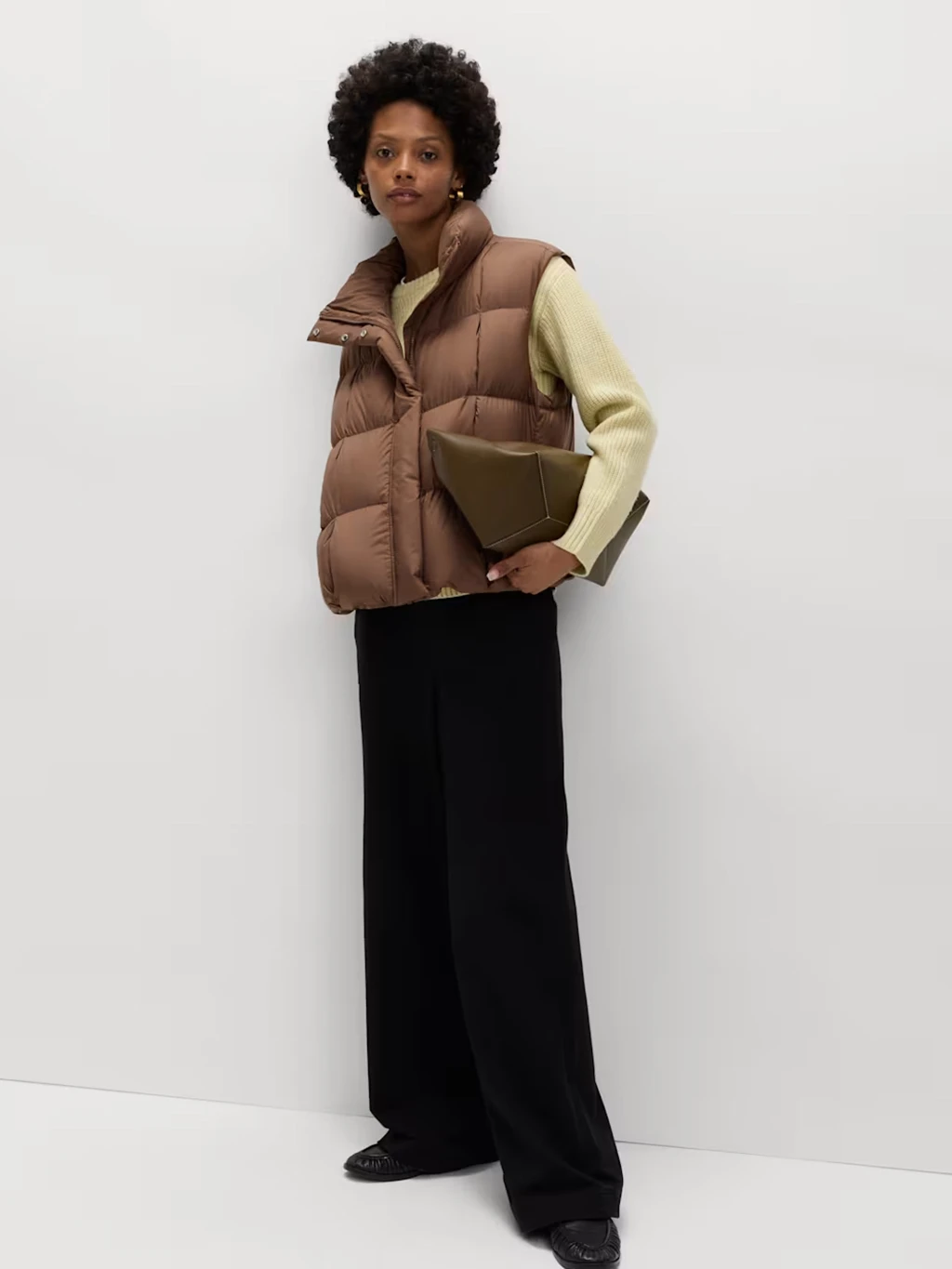 Woman wearing black trousers, a yellow jumper and brown padded gilet.