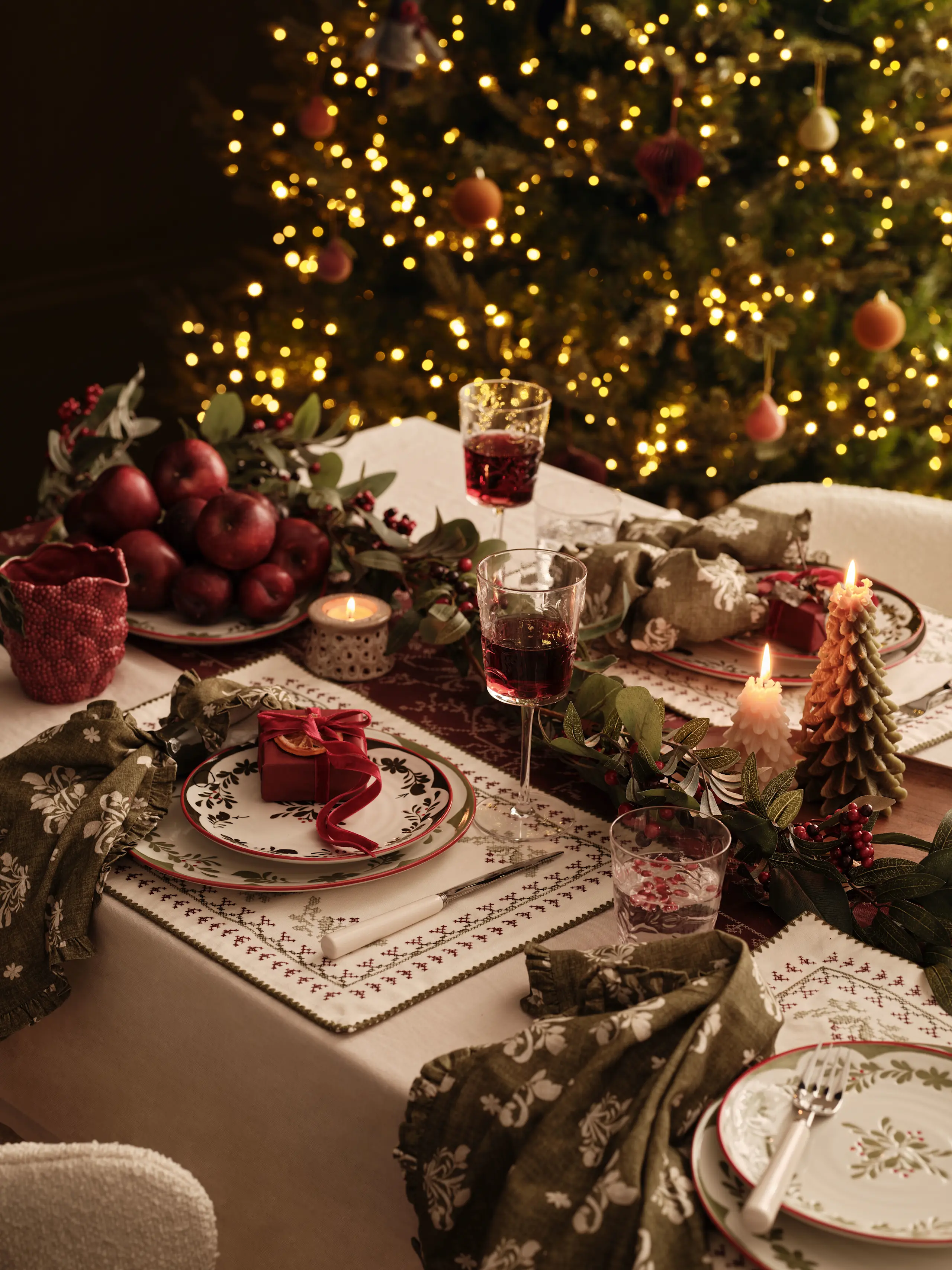 Image of cosy festive table deco including Christmas lights, wine glasses, foliage and plates
