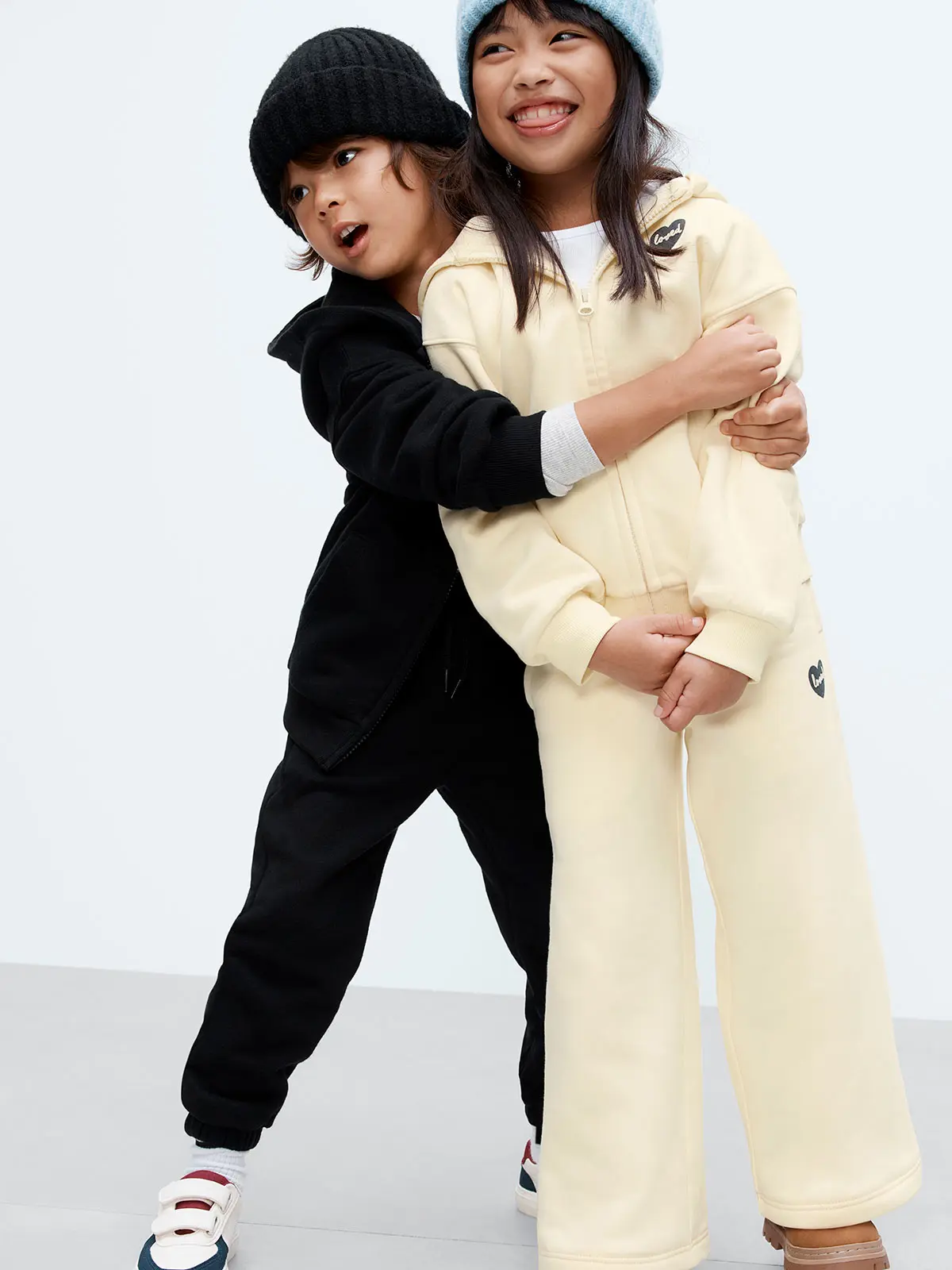 Boy in black hoodie and joggers hugging girl wearing butter yellow hoodie and joggers