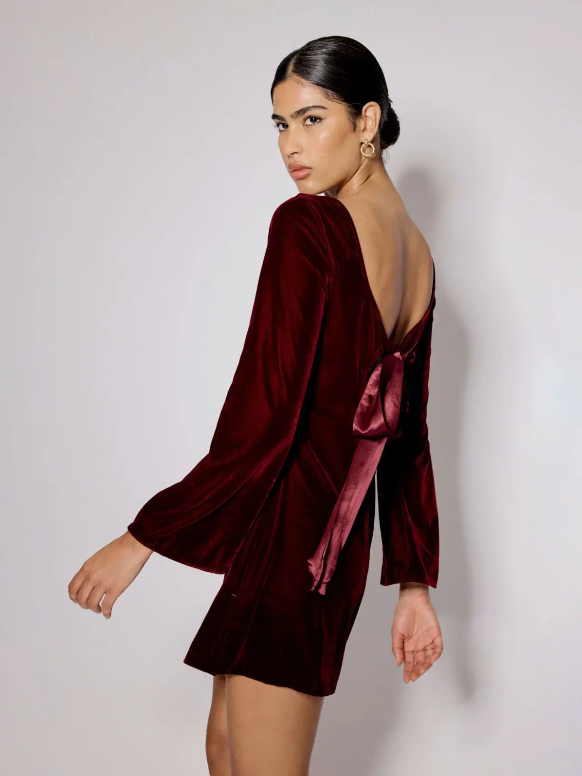 Woman wearing burgundy velvet mini dress with low back and bow detail