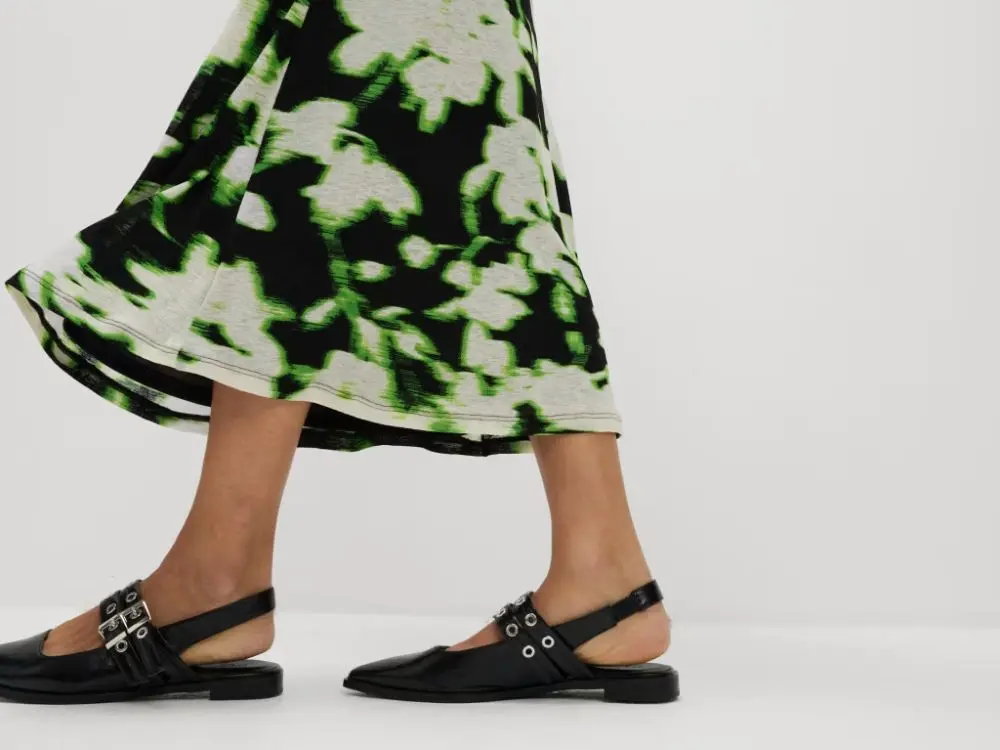 A close up of someone wearing black studded ballet pumps and a green, white and black midi skirt