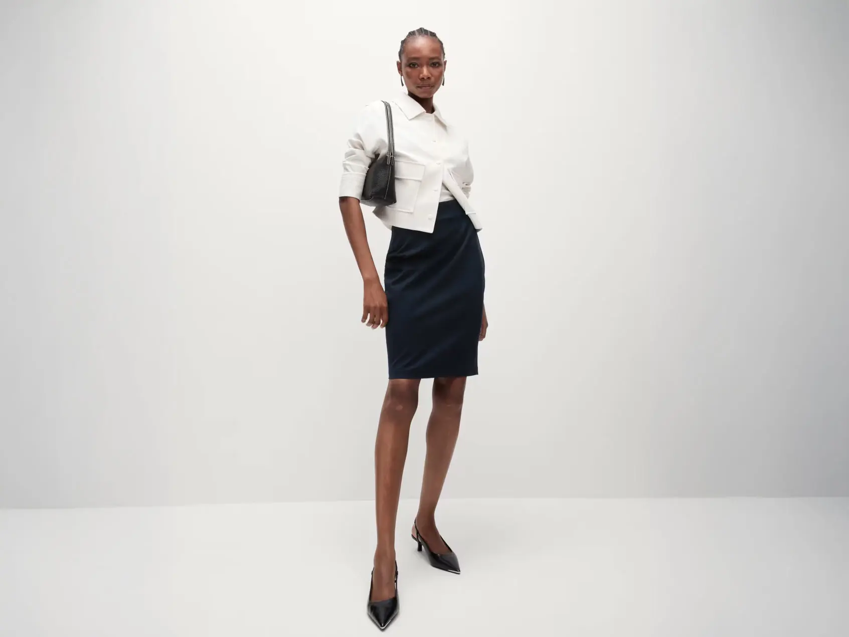 Woman wearing a black pencil skirt with a white top and jacket, black heels and a handbag