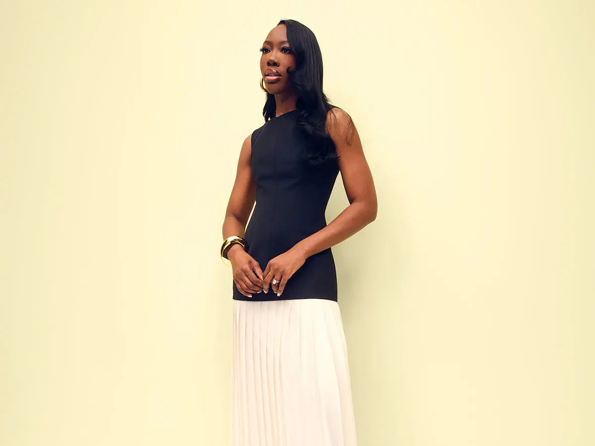 Woman in black sleeveless top and neutral pleated skirt 